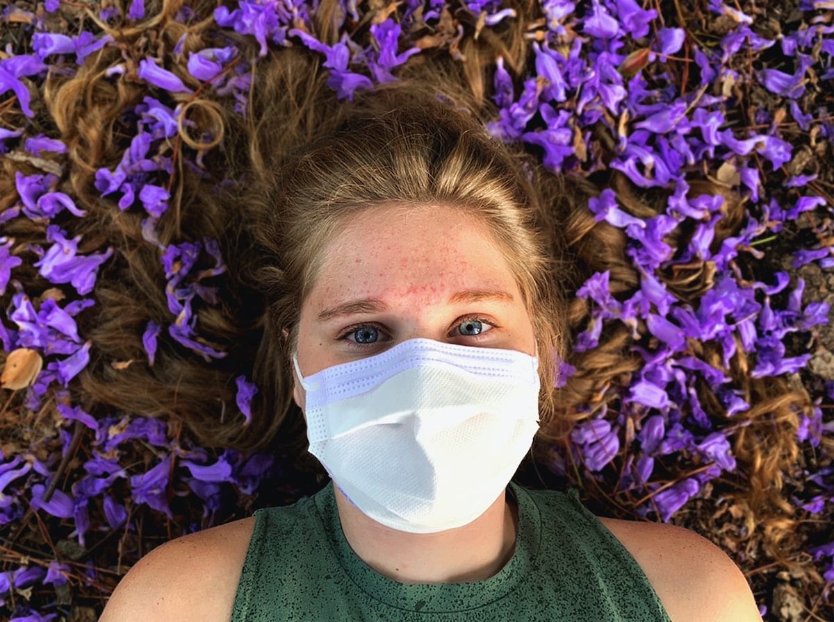 A woman wears a mask as she lies in a bed of flowers.The environmental impacts of COFIC-19 is an opportunity to reconsider our relationship with the planet.
